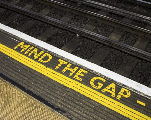Mind the gap sign on the floor of a London Underground station with a railway line beyond
