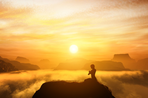 Peace of mind - Woman meditating, sitting in a yoga position on the top of a mountain above clouds at sunset.